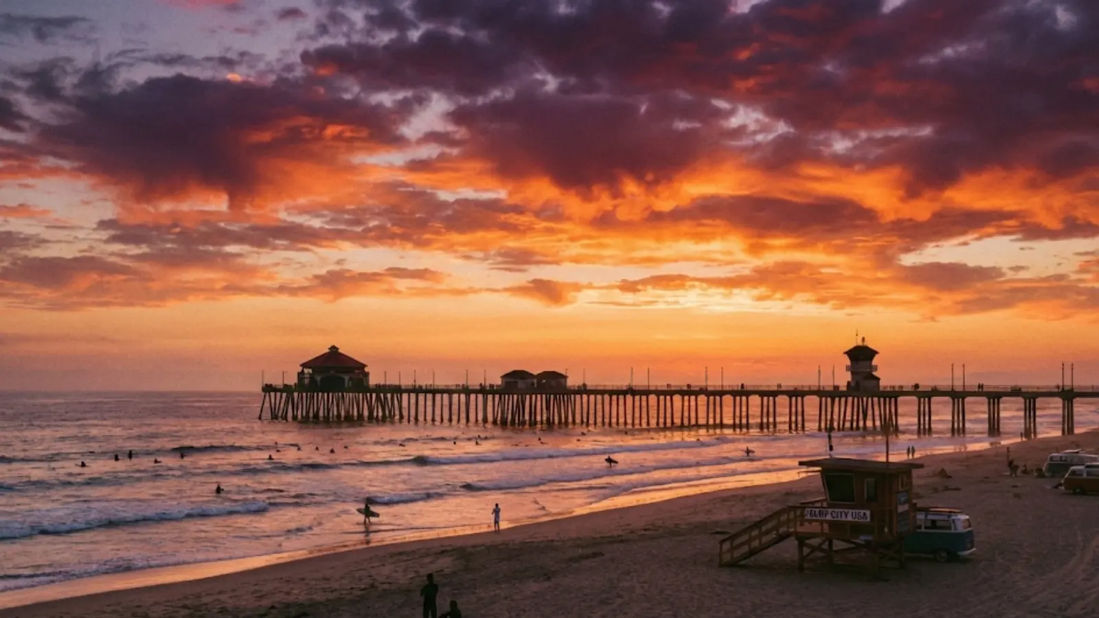 Silhouette of surfers near Huntington Beach Pier during a vibrant sunset.